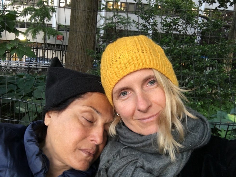 two individuals wearing warm hats in a leafy outdoor setting