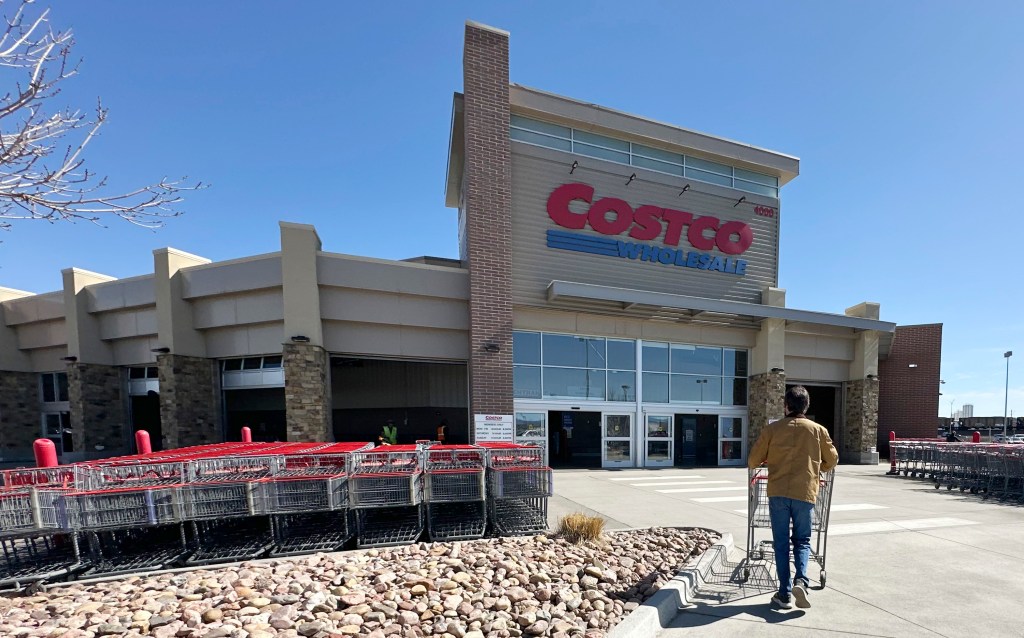 A person pushes a shopping cart toward the entrance of a Costco warehouse.