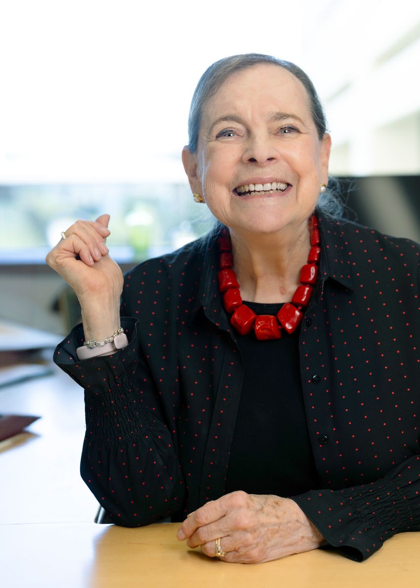 A photograph of developmental biologist Lucy Shapiro, who helped establish the field of systems biology, wearing a black top and red necklace.