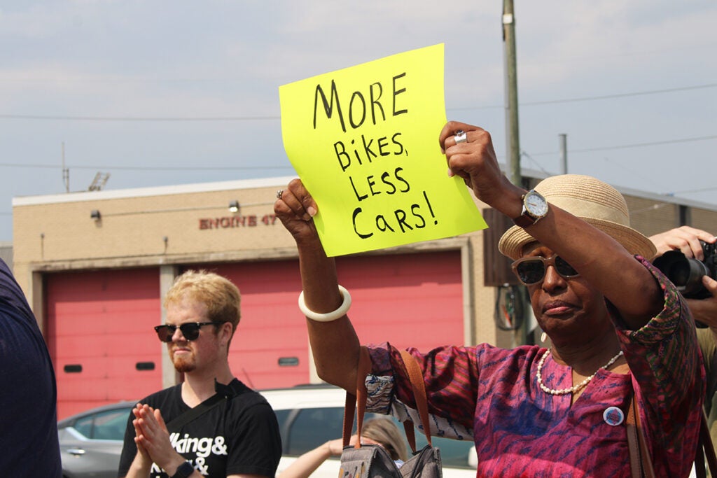 A woman holds a sign that reads "more bikes less cars"
