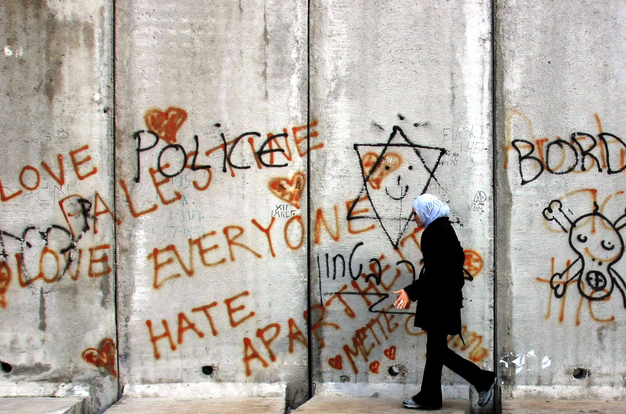 A Palestinian woman wearing a headscarf walks along a concrete barrier covered with graffiti, including messages of peace and protest, in the West Bank town of Abu Dis near Jerusalem.