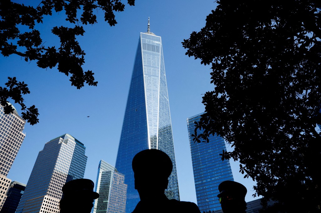 Silhouetted figures at the 9/11 Memorial & Museum with One World Trade Center in the background.