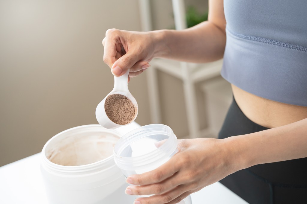 woman pouring protein powder into a cup to make replacement food meal after workout