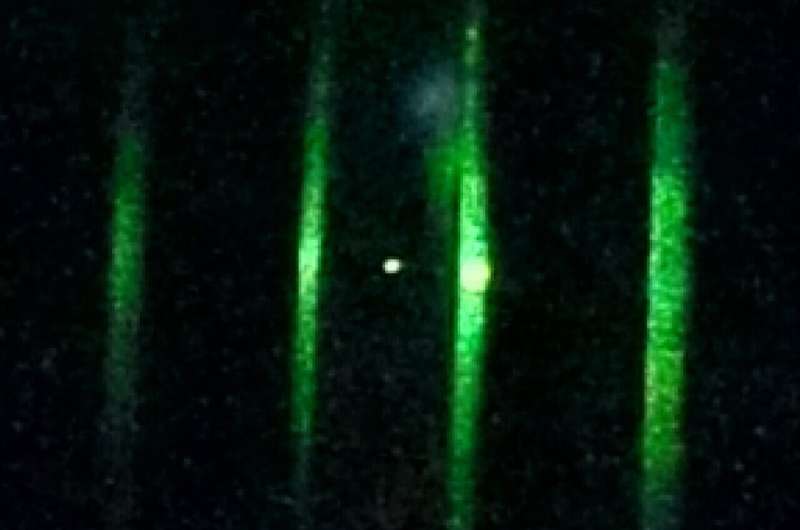 A single nanoparticle made of glass (a white point near the center of the photo) is confined in an optical potential created with a focused laser beam. By detecting the light scattered by the nanoparticle, researchers measured its center-of-mass motion. Credit: Science (2025). DOI: 10.1126/science.ady4652 "Quantum squeezing" a nanoscale particle for the first time