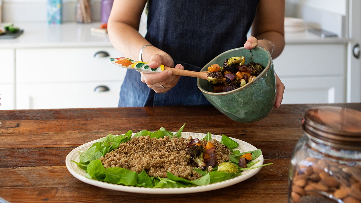 Woman prepared quinoa on a bed of spinach with roasted veggies as an idea for protein-packed meals that don't eliminate carbs and can help lose weight and build muscle