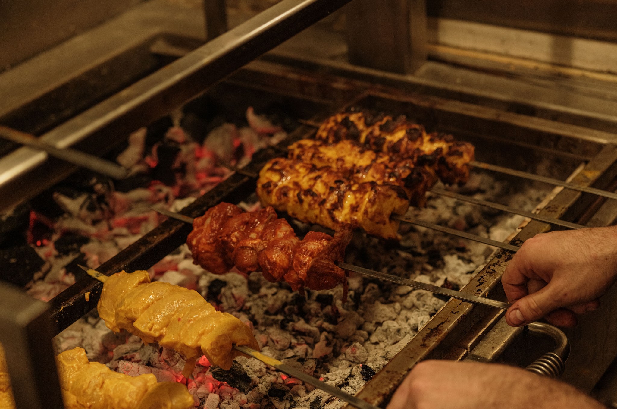 Outstretched hand turning kebabs above a fire.
