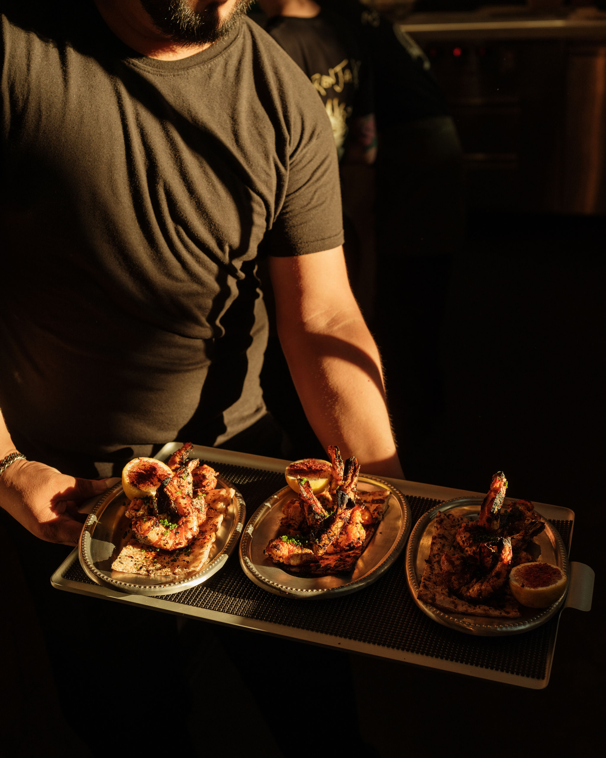 Server holding a tray of small plates against a stark black backdrop.
