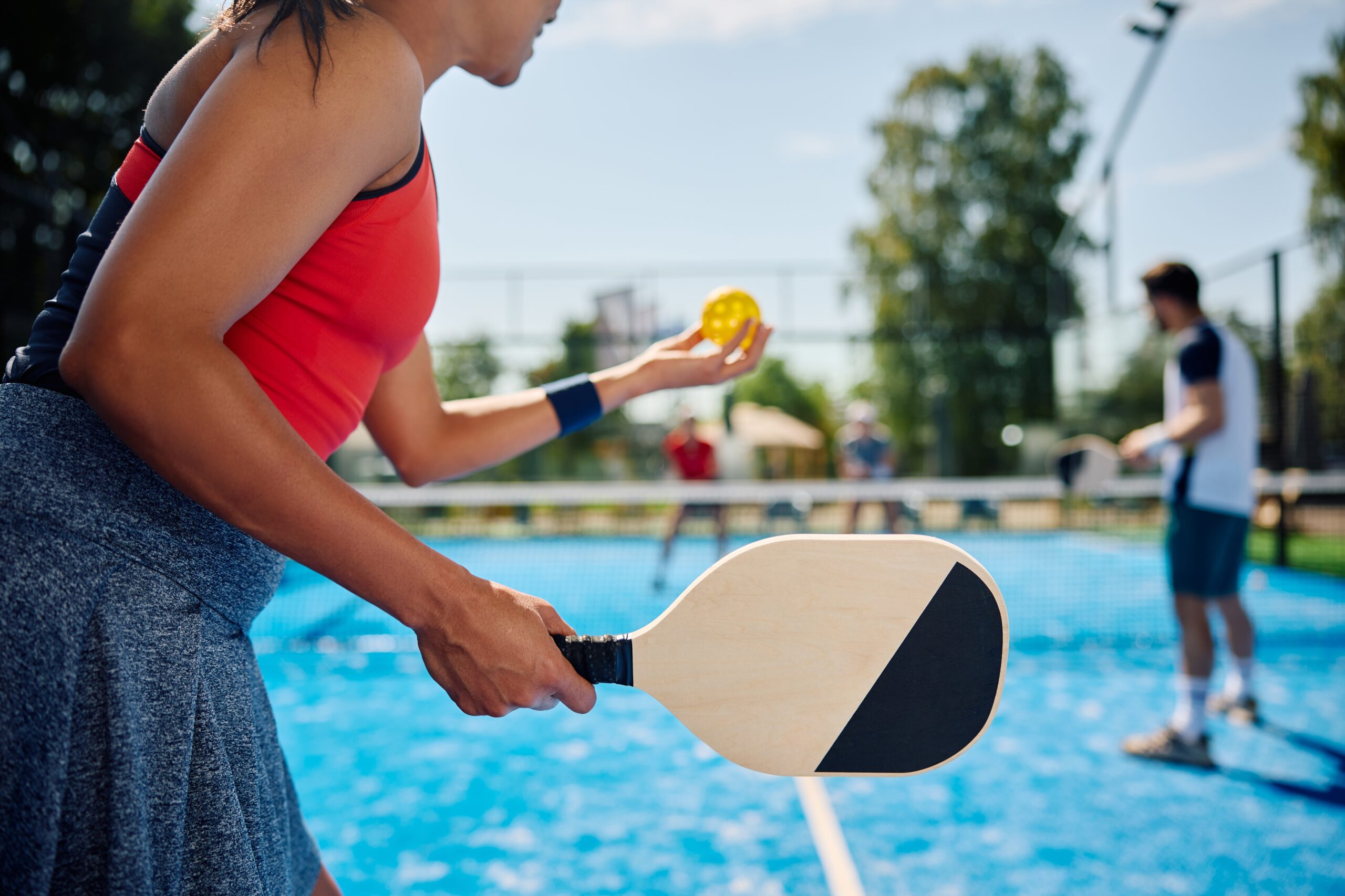 A woman holding a black and white paddle about to hit a yellow ball