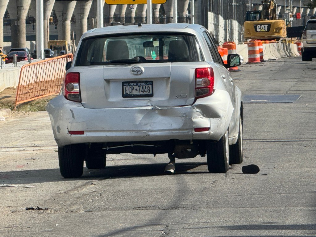 A silver car with a severely damaged rear bumper and a New York license plate ECP-7448.