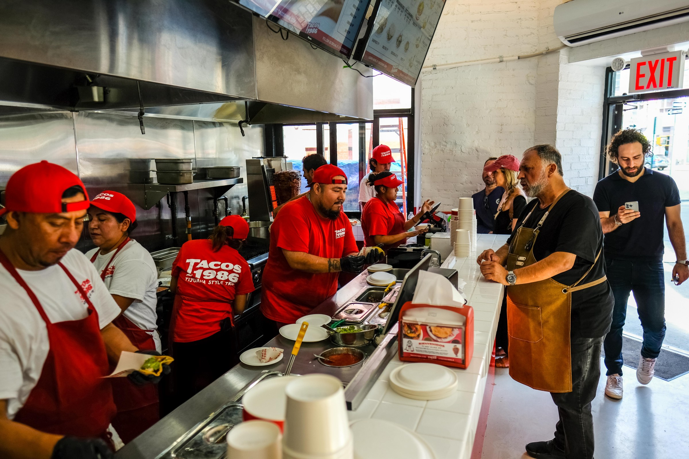 A restaurant taco counter with people behind the counter and someone ordering food.