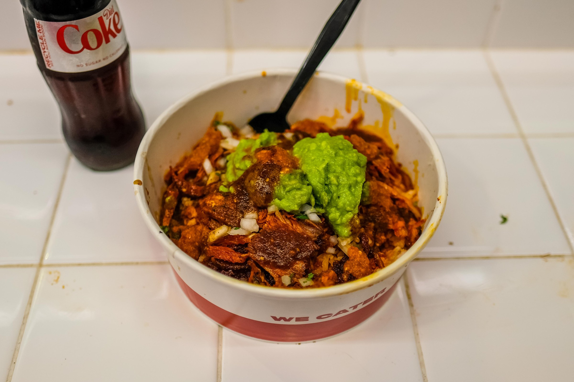A cardboard container of beans and rice with guacamole.