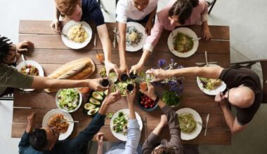 An aerial view of a table laden with vegan food and a group of people raising their glasses in a toast.