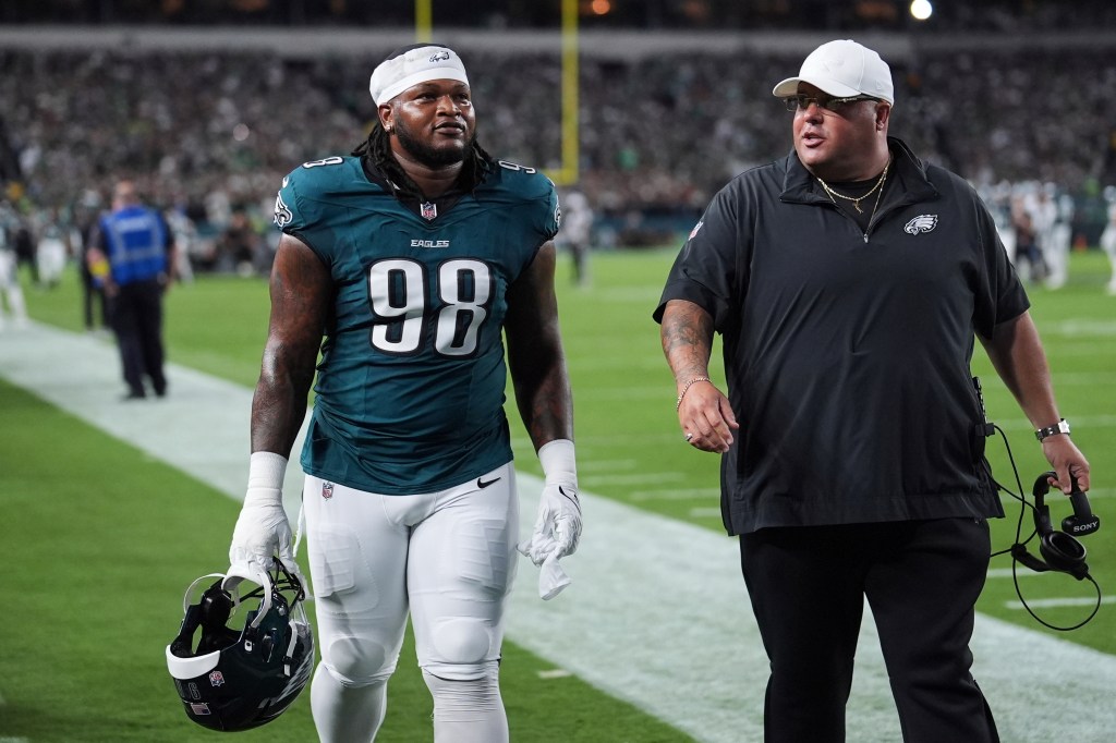 Philadelphia Eagles player Jalen Carter (98) walks off the field with a coach.