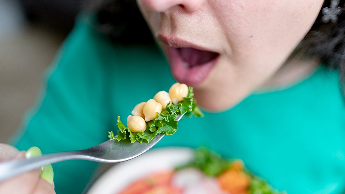 A woman is about to eat chickpeas on a fork.