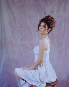A dark-haired woman poses in a white short dress.