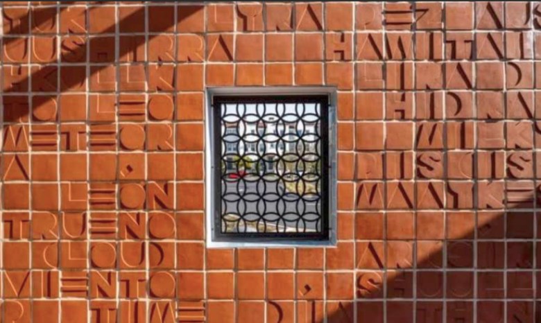 a terra cotta backdrop designed in squares that display letters to spell out words. A see-through panel in the enter allows for a view.