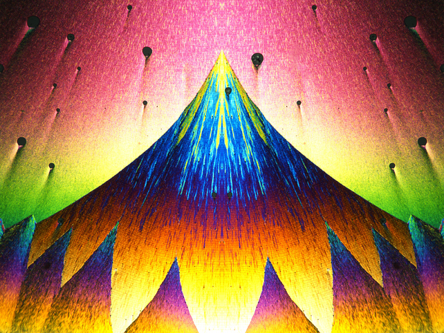 Multicoloured pattern of triangular shapes with one large volcano-like triangle at the centre, bearing streaks of yellow and blue, and a row of smaller triangles along the bottom edge with yellow-orange bases, purple midlines and blue-green tips. There are oddly spaced black dots on the pink-yellow background in the top third of the image. 