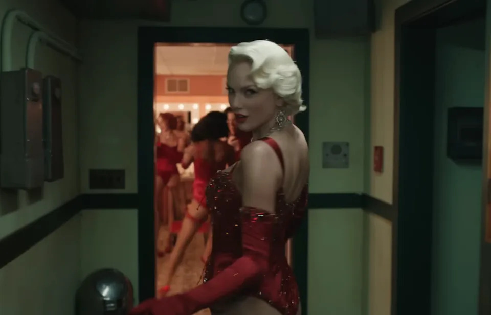 Person in vintage, glamorous attire with elegant gloves and styled hair, walking through a backstage hallway
