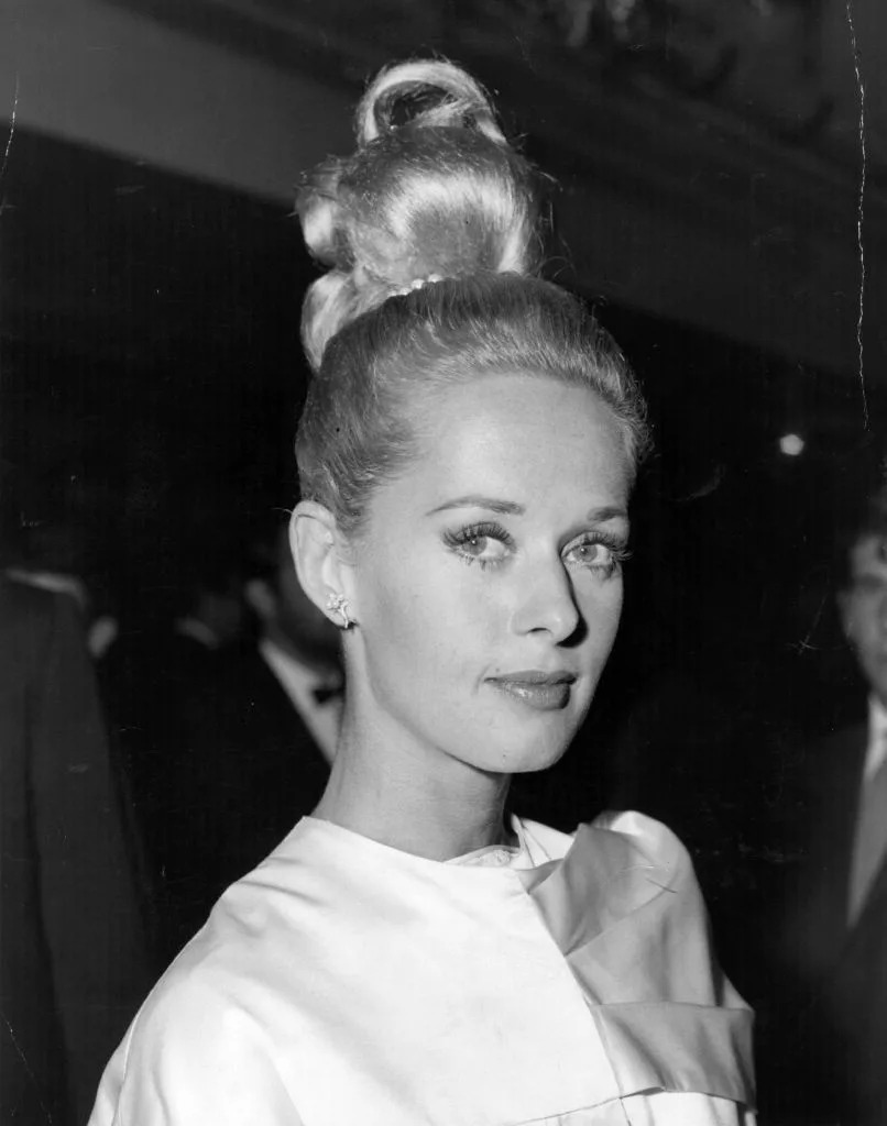 Person in elegant evening attire with high updo hairstyle, looking at the camera at a formal event