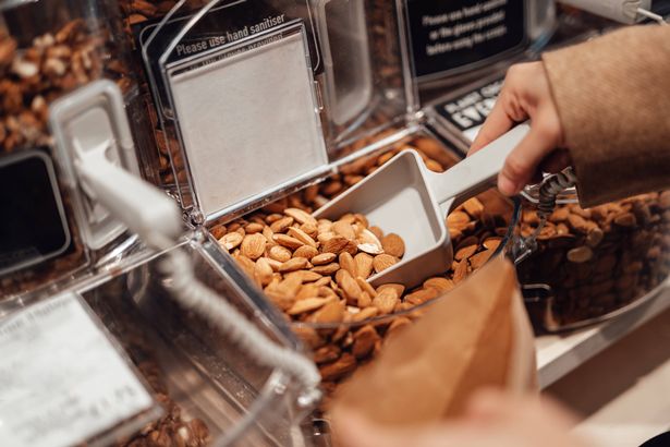 Close up shot of woman using scoop to refill store dispensing almond into paper bag in local organic whole foods refill store.