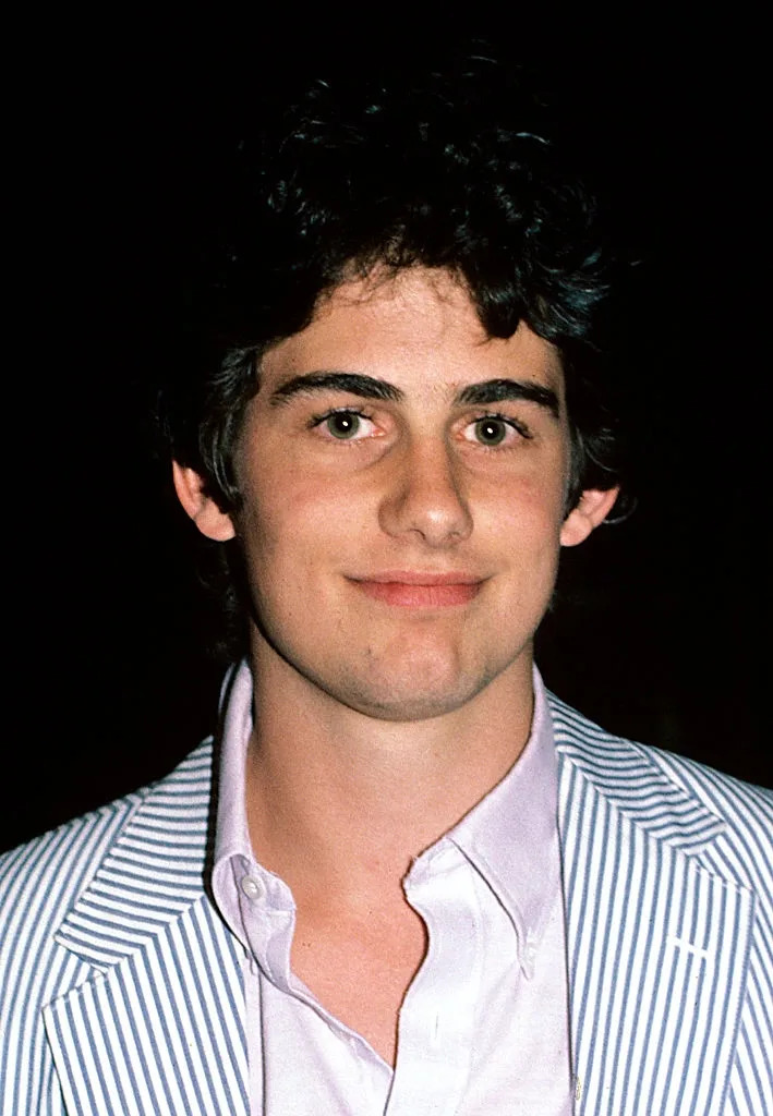 A person wearing a pinstripe blazer over a collared shirt smiles at the camera