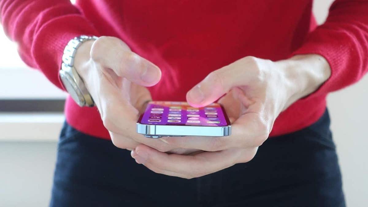 A person in a red sweater holds a smartphone with a colorful home screen, typing on the device.