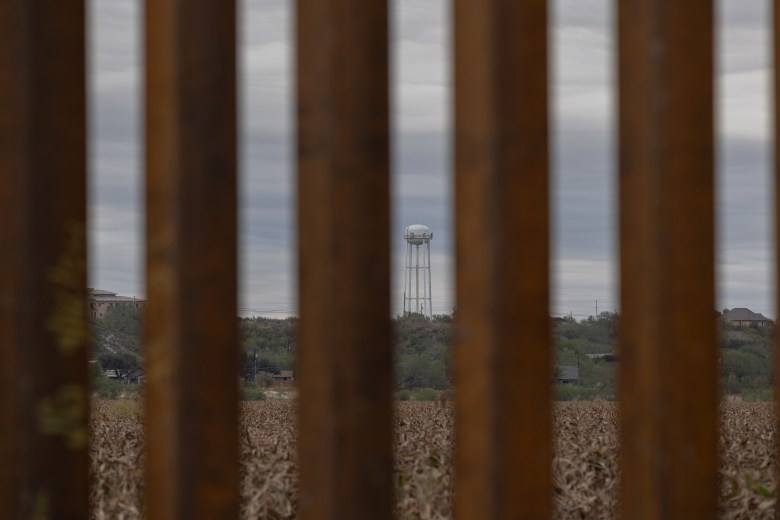 A water tower and a neighborhood are visible through border wall slats in Rio Grande City on Nov. 26, 2024.