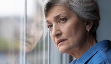 Close up head shot frustrated middle aged 60s woman standing near window, looking in distance, feeling depressed indoors.
