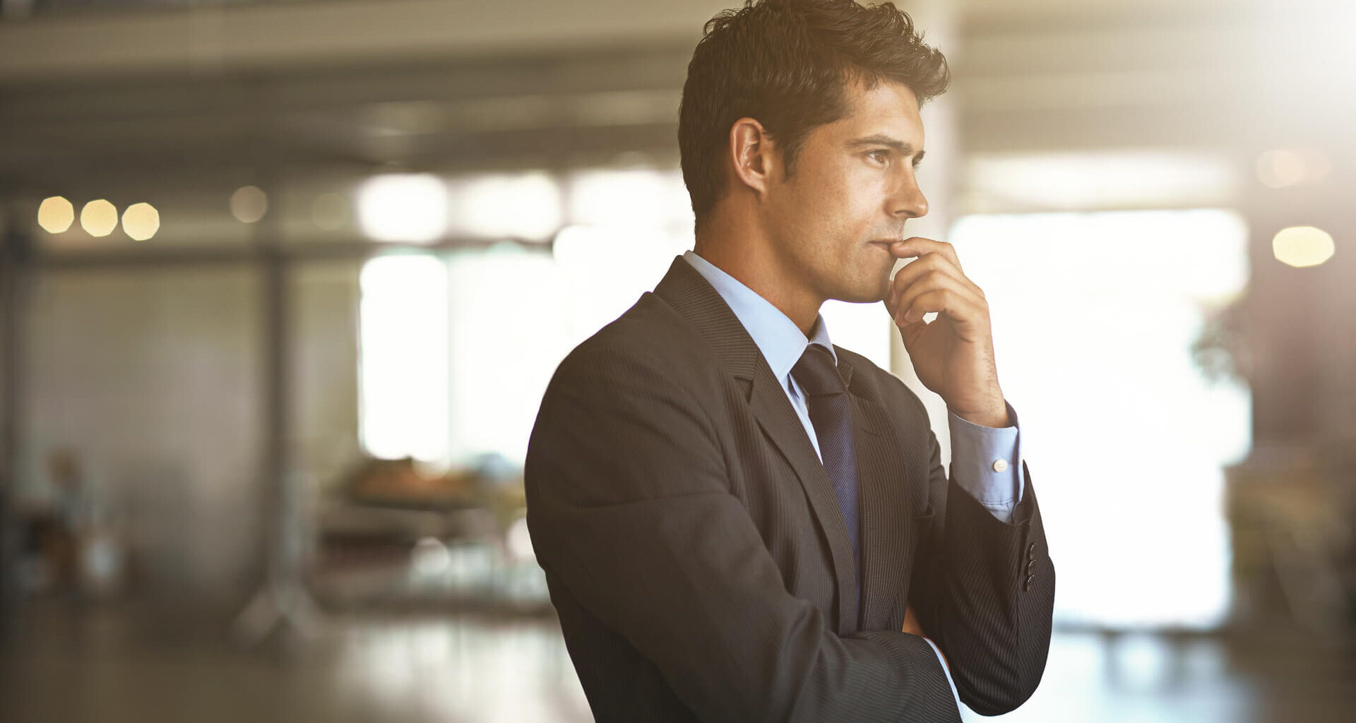 A successful businessman thinking while standing inside his company contemplating his wealth and money moves.
