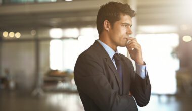 A successful businessman thinking while standing inside his company contemplating his wealth and money moves.