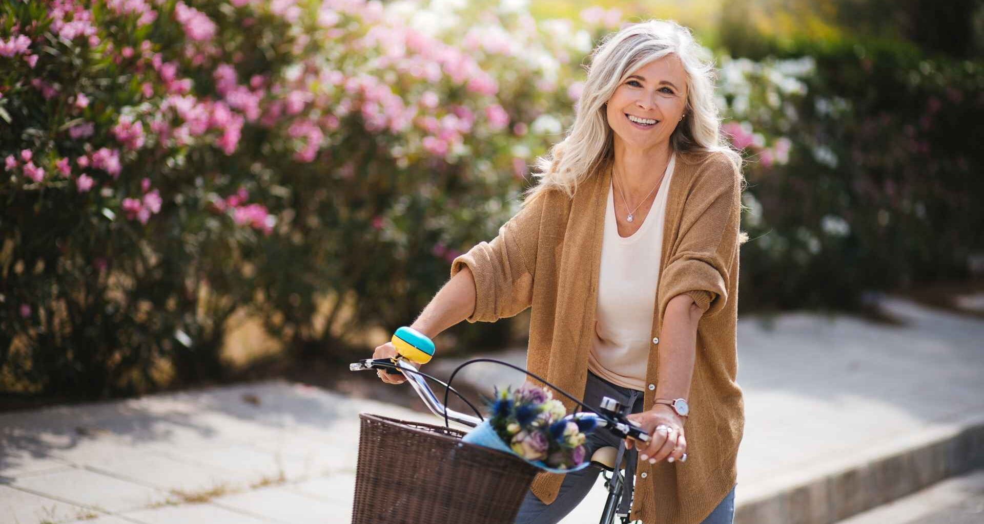 Happy active mature woman in fashionable clothes riding bicycle on suburban neighborhood street in spring.