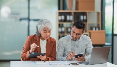 Senior Asian business woman and young man working together analyzing finances senior staff teach marketing and planning to younger staff woman holding graph and chart with a happy smile.