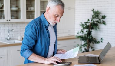 Focused senior man using a calculator and a laptop.