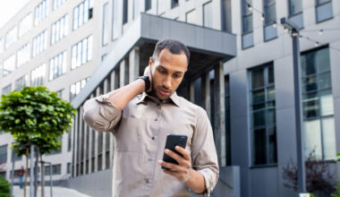 Disturbed arab man rubbing head with hand while looking at mobile phone screen on background of office building, investing myths, losing money