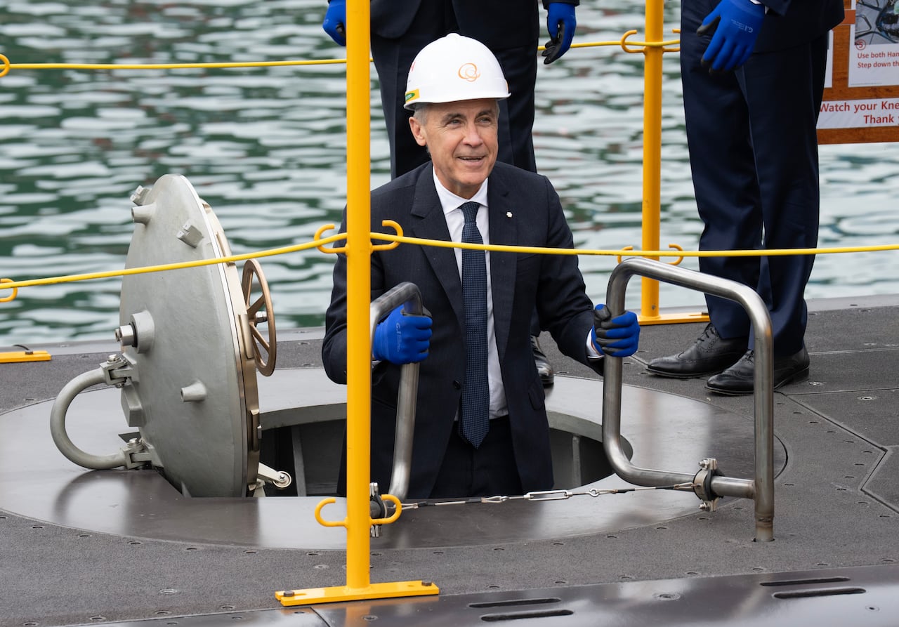 A man in a suit wearing a hard hat is seen popping out the top of a submarine.