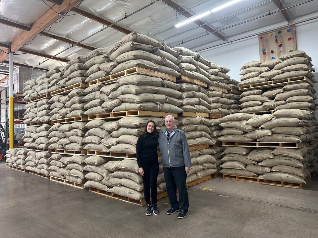 Woman and man standing in front of pallets stacked with bags of coffee.