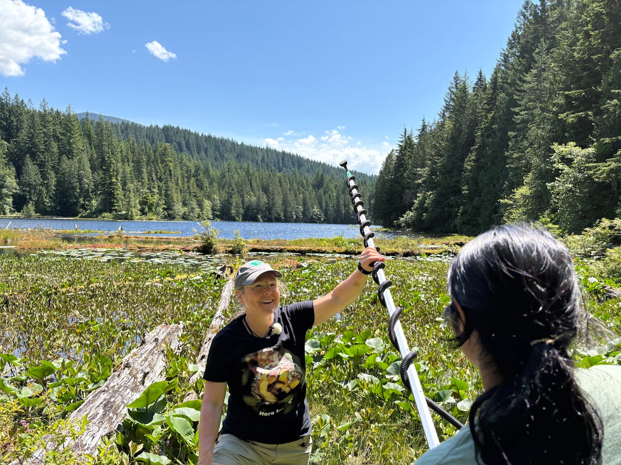 A woman holds up some research equipment near a river.