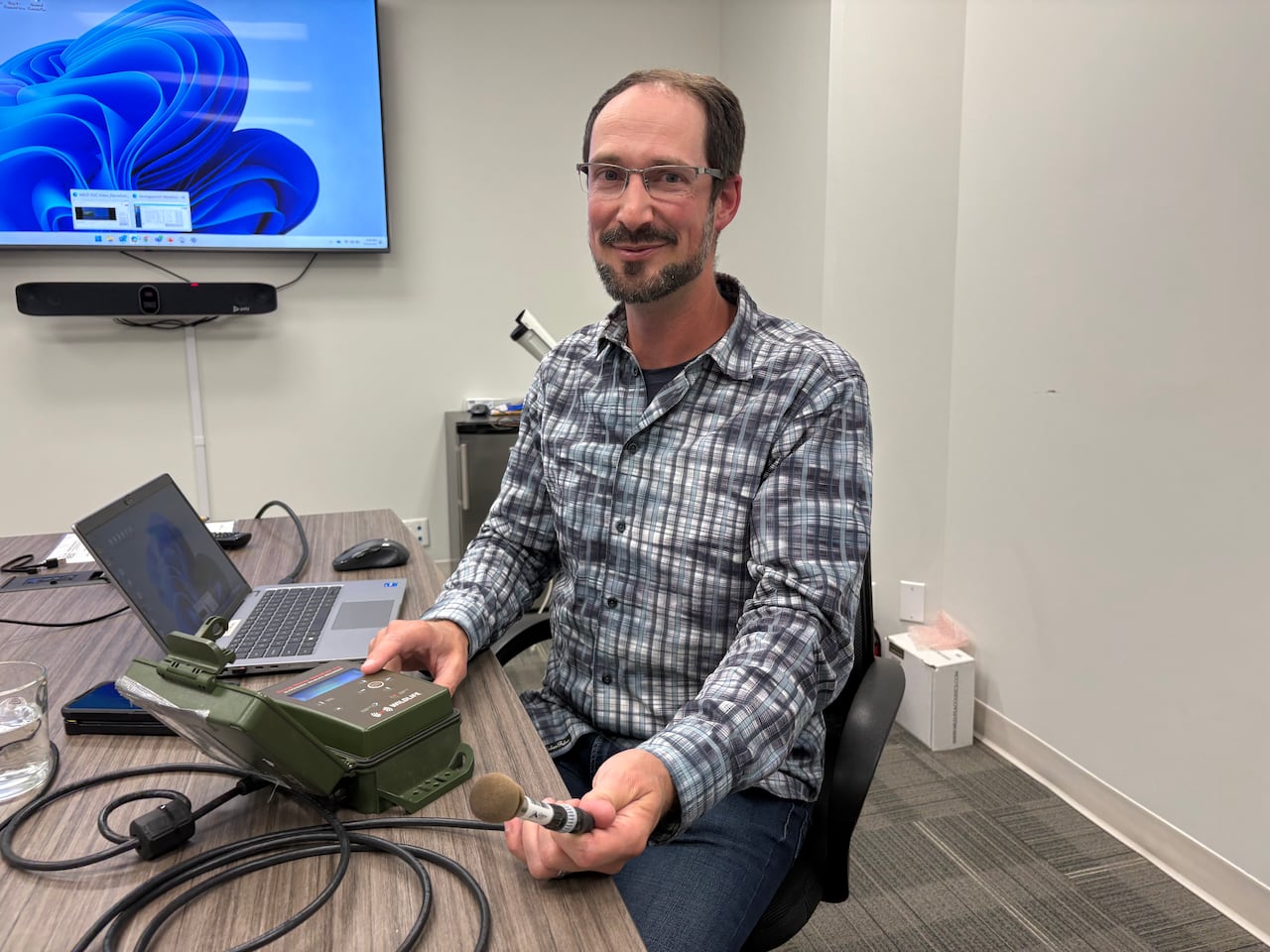 A man holds on to recording equipment while sitting at a table.