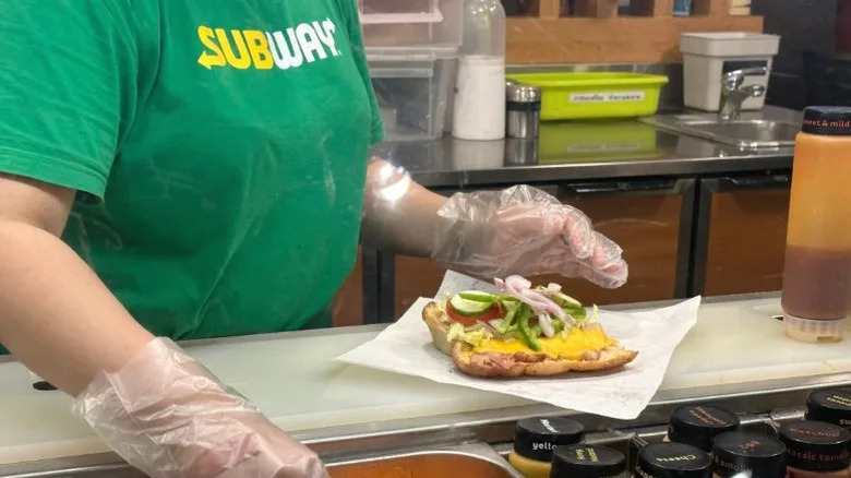 A Subway sandwich maker preparing a sandwich.