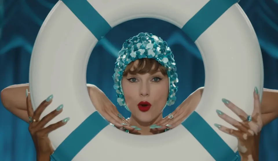 Woman wearing a sequin swim cap poses playfully with a life preserver, her nails and accessories matching the cap