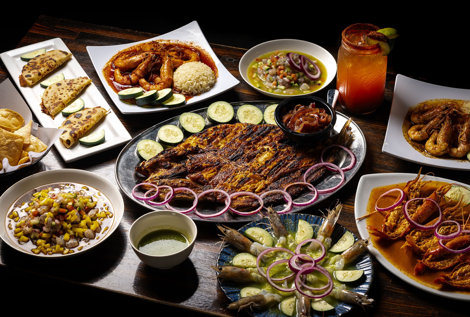 The entire array of Mexican seafood dishes on a wooden table with grilled fish, shrimp of all kinds, and a Michelada.