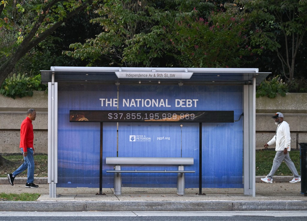 A bus stop shelter with "THE NATIONAL DEBT" and "$37,855,195,989,869" displayed on it.