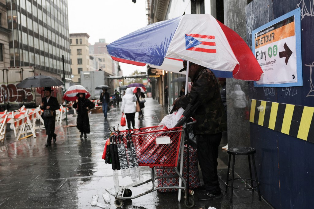 A vendor selling umbrellas under a Puerto Rican flag umbrella during a rain shower.