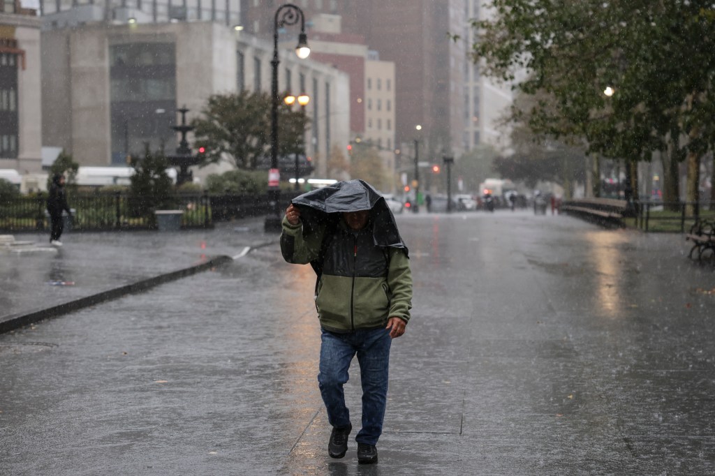 A person walking in the rain holding a jacket over their head in a city street.