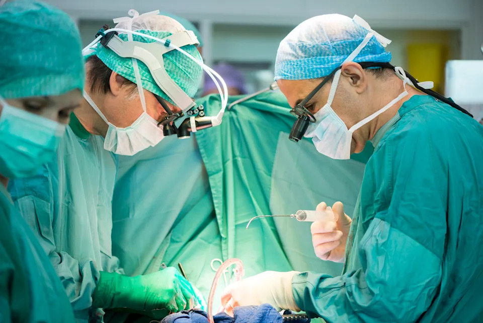 Surgeons in scrubs and masks focus intently during an operation, surrounded by medical equipment and bright lights
