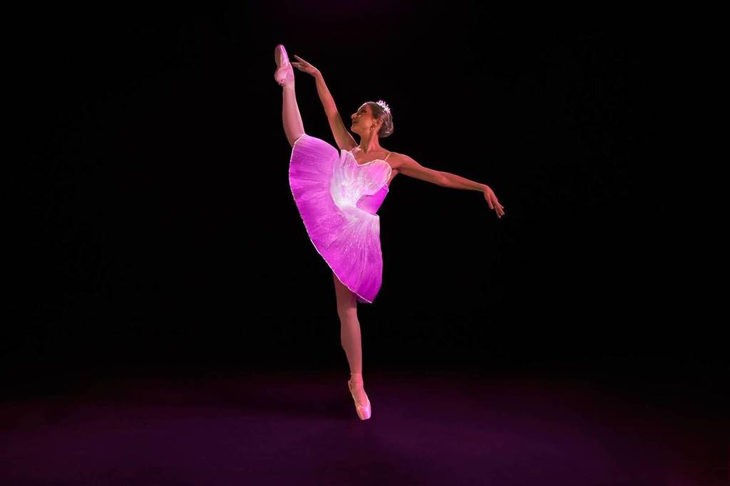 A ballerina in LED-lit costumes in développé