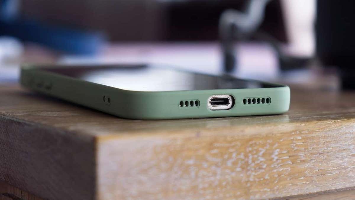 Close-up of a smartphone with a green case resting on a wooden surface, showing its USB-C charging port.