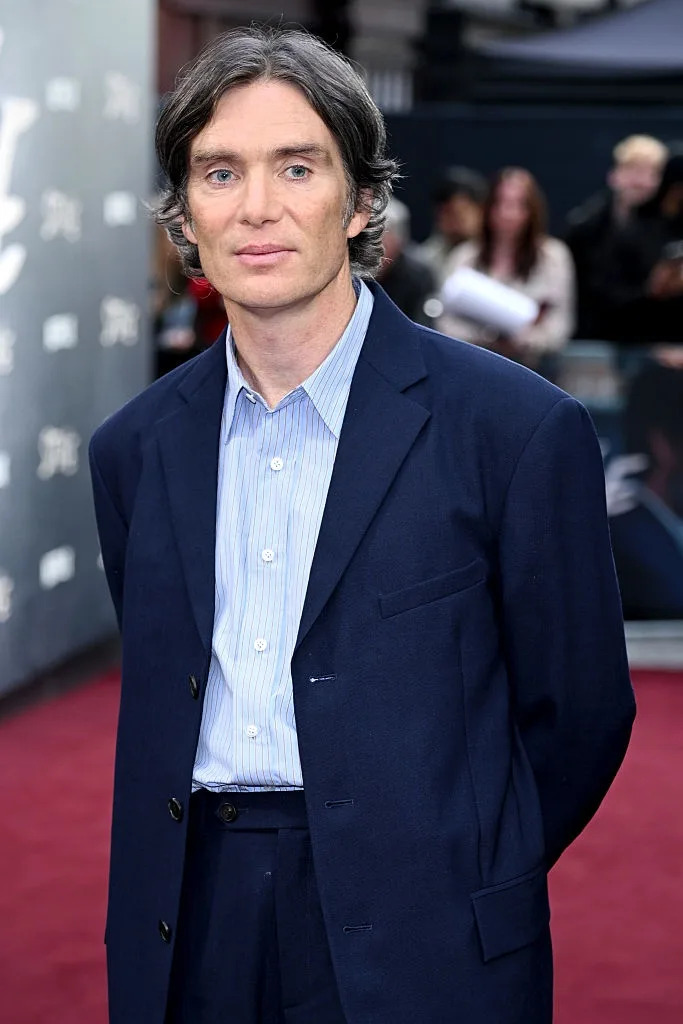 Person on the red carpet in a blue suit with a light striped shirt, posing for photos