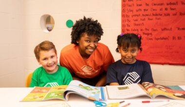 Two smiling children and one staff member reading books at the Boys & Girls Club