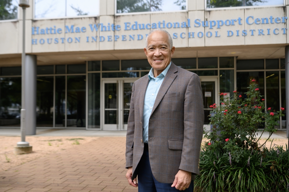 a man in a gray blazer stands in front of an education building